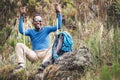 Portrait of a cheerfully smiling African-American Ethnicity young man in sunglasses sitting with a backpack and trekking poles and