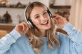 Portrait of cheery blond girl 20s wearing headphones listening to music at home Royalty Free Stock Photo