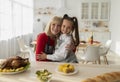 Portrait of cheery little girl and her grandmother in aprons cooking Christmas dinner, posing and hugging in kitchen Royalty Free Stock Photo