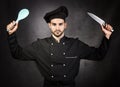 Portrait of a chef cooker with knife and spoon in black uniform, gray background Royalty Free Stock Photo