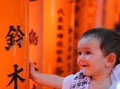 Portrait of a cherful little baby with red colorful toriis of Fushimi Inari Taisha shrine on background.