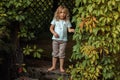 Portrait of cherubic barefoot little girl standing on old stairs in wooden ivy-covered gazebo, playing hide-and-seek.