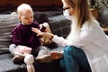 Cherubic blond little girl toddler sitting on sofa, giving brown bottle to childrens doctor examining patient at home.