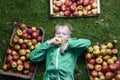 Portrait of Child blond boy lying on the green grass background with pile of apples, holding and eating apple Royalty Free Stock Photo