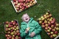 Portrait of Child blond boy lying on the green grass background with pile of apples, holding and eating apple Royalty Free Stock Photo