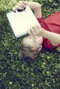 Portrait of Child blond young boy playing with a digital tablet computer outdoors lying on grass Royalty Free Stock Photo