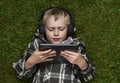 Portrait of Child blond young boy playing with a digital tablet computer outdoors lying on grass Royalty Free Stock Photo