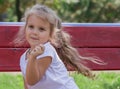 Cheerful little girl 4 years old, blonde with long flowing hair, sits on a park bench Royalty Free Stock Photo