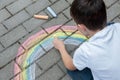 Portrait of a child drawing a rainbow on the street with colored chalk. Selective focus. Kid. A child is playing outside Royalty Free Stock Photo