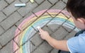 Portrait of a child drawing a rainbow on the street with colored chalk. Selective focus. A child is playing outside Royalty Free Stock Photo