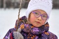 Portrait of a child girl in glasses on a winter walk. The girl is dressed in a hat and jacket. A cloudy winter day. Royalty Free Stock Photo