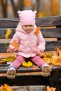 Portrait of a child girl sitting on a bench in autumn city park and playing with maple leaves. Beautiful nature, trees with yellow Royalty Free Stock Photo