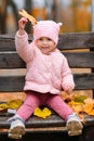 Portrait of a child girl sitting on a bench in autumn city park and playing with maple leaves. Beautiful nature, trees with yellow Royalty Free Stock Photo