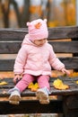 Portrait of a child girl sitting on a bench in autumn city park and playing with maple leaves. Beautiful nature, trees with yellow Royalty Free Stock Photo