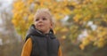 Portrait of child at nature at autumn day against yellowed trees, weeknd walk in park, medium shot