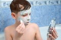 Portrait of child teen boy removing alginate mask from face looking at mirror.