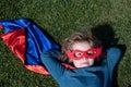 Portrait of child wearing a superhero costume laying on grass. Super hero child having fun in park outdoors. Kids power Royalty Free Stock Photo