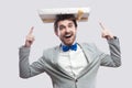 Portrait of childish funny young man in gray coat and blue bow tie standing and pointing fingers to present on his head, toothy Royalty Free Stock Photo