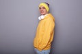 Portrait of childish playful shocked man wearing yellow hoodie, beanie hat and headphones standing isolated over gray background, Royalty Free Stock Photo