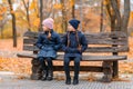 Portrait of a children in an autumn city park - happy people sitting together on a wooden bench, posing against a background of Royalty Free Stock Photo