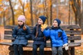 Portrait of a children in an autumn city park - happy people sitting together on a wooden bench, posing against a background of Royalty Free Stock Photo