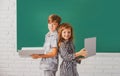 Portrait of children boy and girl with laptop computer and book at school. Kids in class on blackboard. Royalty Free Stock Photo