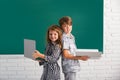 Portrait of children boy and girl with laptop computer and book at school. Kids in class on blackboard. Royalty Free Stock Photo