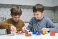 Portrait of children friends sitting at table in kitchen at home, reading instruction for playing construction blocks.