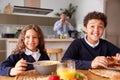 Portrait Of Children Wearing School Uniform Eating Breakfast As Father Gets Ready For Work Royalty Free Stock Photo