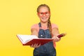 Portrait of clever creative little girl in red glasses holding notebook and pencils, school child smiling at camera