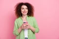 Portrait of clever girl with wavy hairdo wear green shirt look at eshop empty space hold smartphone isolated on pink