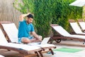 Portrait of clever handsome bearded young adult freelancer man in blue t-shirt and shorts sitting on cozy deck chair with laptop Royalty Free Stock Photo