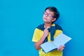 Portrait of a clever and studious boy with red glasses, with a yellow shirt and a sweater on his shoulders, holding a pencil and a Royalty Free Stock Photo