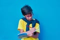 Portrait of a clever and studious boy with red glasses, with a yellow shirt and a sweater on his shoulders, holding a pencil and a Royalty Free Stock Photo