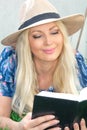 Portrait close-up. Beautiful blonde young woman in a hat is lying on the grass and reading a book. Royalty Free Stock Photo