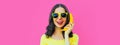 Portrait close up of funny young woman calling on banana phone on pink background