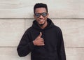 Portrait of happy smiling young african man showing thumbs up wearing a black hoodie, sunglasses on a city street over