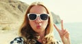 Portrait close up happy young woman blowing her lips sending sweet air kiss stretching hand for taking selfie on a sea and Royalty Free Stock Photo