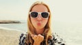 Portrait close up of happy young woman blowing her lips sending sweet air kiss stretching hand for taking selfie on sea background Royalty Free Stock Photo