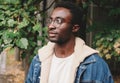 Portrait close-up modern african man thinking and looking away wearing eyeglasses in autumn city park on background Royalty Free Stock Photo