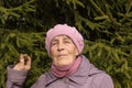 Portrait close-up of a pensioner aged 77 in front of the tree. An elderly woman in a beret and scarf.