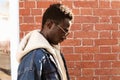 Portrait close up side view stylish african man wearing sunglasses and jeans jacket with hood on city street Royalty Free Stock Photo