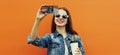 Portrait close up smiling woman taking a selfie picture by smartphone wearing a denim jacket on an orange background Royalty Free Stock Photo