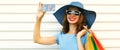 Portrait close up of smiling young woman taking selfie picture by smartphone with shopping bags wearing blue summer straw hat Royalty Free Stock Photo