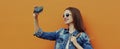 Portrait close up smiling young woman taking a selfie picture by smartphone wearing a denim jacket on a orange background Royalty Free Stock Photo