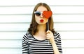 Portrait close-up woman blowing red lips sending sweet air kiss hiding her eye with red heart shaped lollipop on white wall Royalty Free Stock Photo