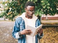 Portrait of young african man student reading a book wearing an eyeglasses in autumn city park Royalty Free Stock Photo