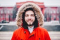 Portrait, close-up of a young stylishly dressed man smiling with a beard dressed in a red winter jacket with a hood and fur on his Royalty Free Stock Photo