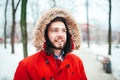 Portrait, close-up of a young stylishly dressed man smiling with a beard dressed in a red winter jacket with a hood and fur on his Royalty Free Stock Photo