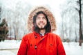 Portrait, close-up of a young stylishly dressed man smiling with a beard dressed in a red winter jacket with a hood and fur on his Royalty Free Stock Photo